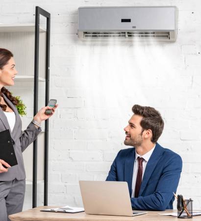 smiling businesswoman holding remote control while standing near handsome manager sitting at